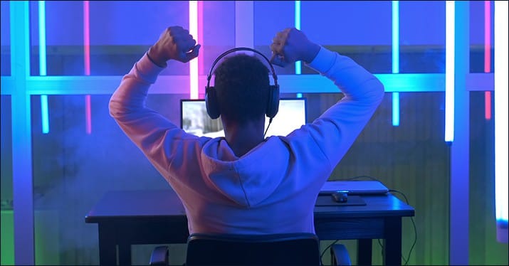 Man using headphones in front of computer with neon lighting, digital music production, streaming, online entertainment, creative content, Hypebot website focus.