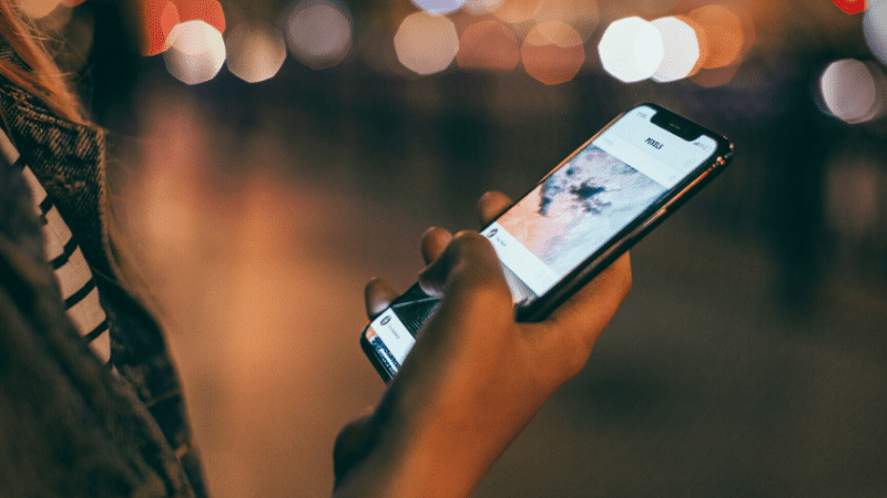 Woman using smartphone at night with blurred city lights in the background.