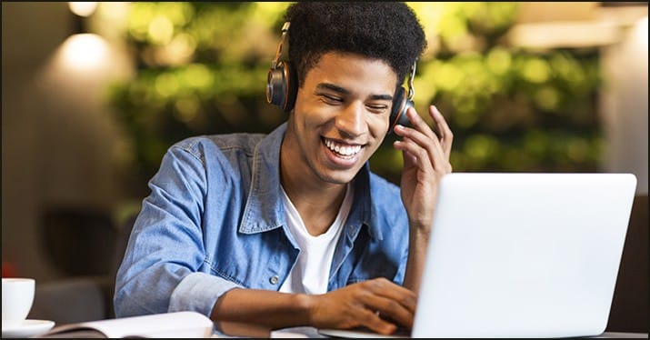 Young man enjoying music with headphones and laptop at a cafe, digital music, streaming, online entertainment, modern technology, casual workspace, happy music lover, remote work, music streaming service, Hypebot.
