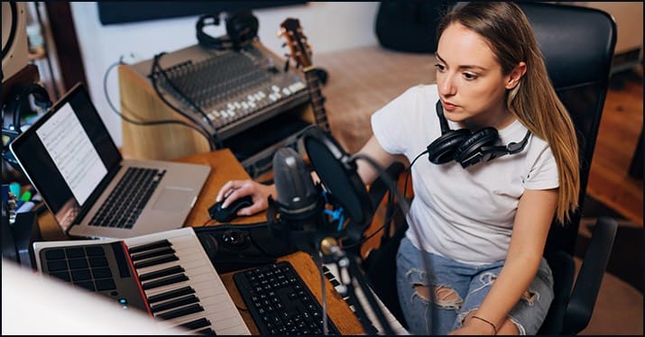 Professional music producer recording in home studio with digital audio workstation, MIDI keyboard, and audio equipment for music industry content creation.