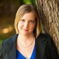 A professional woman with blonde hair wearing a blazer, standing outdoors next to a tree, conveying business confidence and outdoor professionalism, ideal for marketing and business-related content.