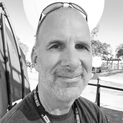 Portrait of a smiling man with sunglasses on his head, outdoors, at a conference or event, representing media, music industry, or entertainment news.