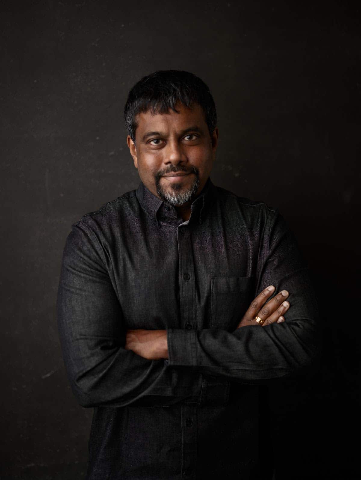 Professional man with crossed arms, dark shirt, posing confidently against black background, representing leadership, confidence, and professionalism in entertainment, media, or creative industries.