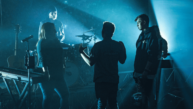 Music band rehearsing during a live concert with stage lighting and musical instruments.