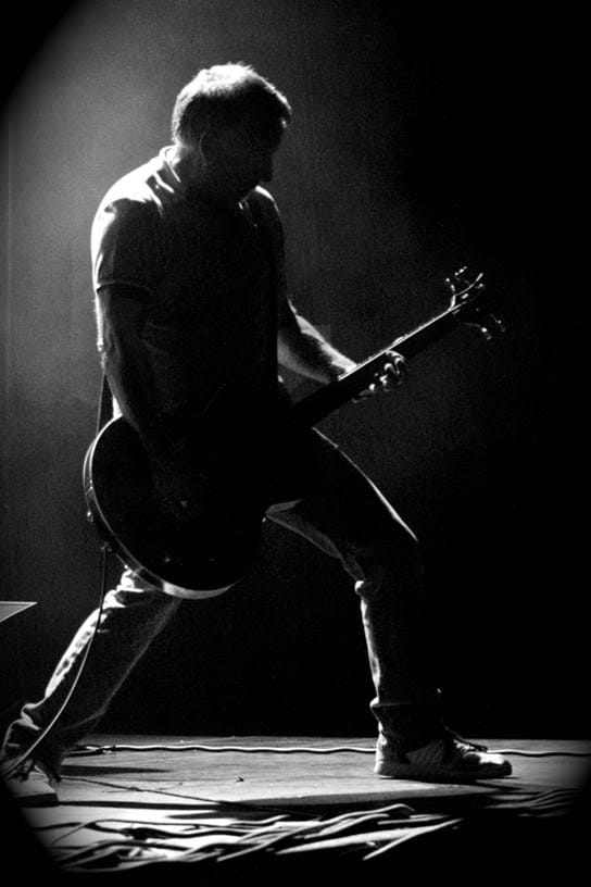 Electric guitarist performing passionately on stage in a dramatic black and white image.