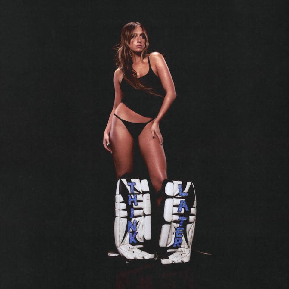 Image of a woman in black sportswear with custom hockey goalie pads labeled "Think" and "Laughter" on a black background. The photo exudes confidence and a bold athletic personality, ideal for promoting sports gear or fitness branding.