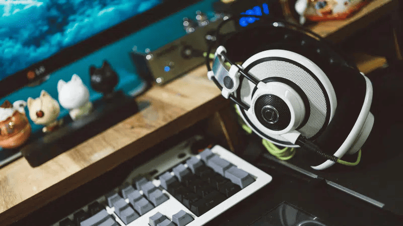 Headphones and gaming setup on wooden desk for music and gaming entertainment.