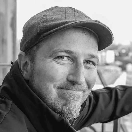 A smiling man wearing a cap outdoors, showcasing a relaxed and approachable demeanor.