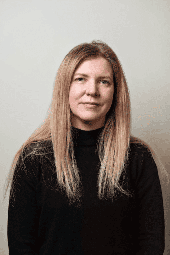 Professional woman with long blonde hair wearing a black top, looking confidently at the camera in a studio portrait for digital marketing or branding.