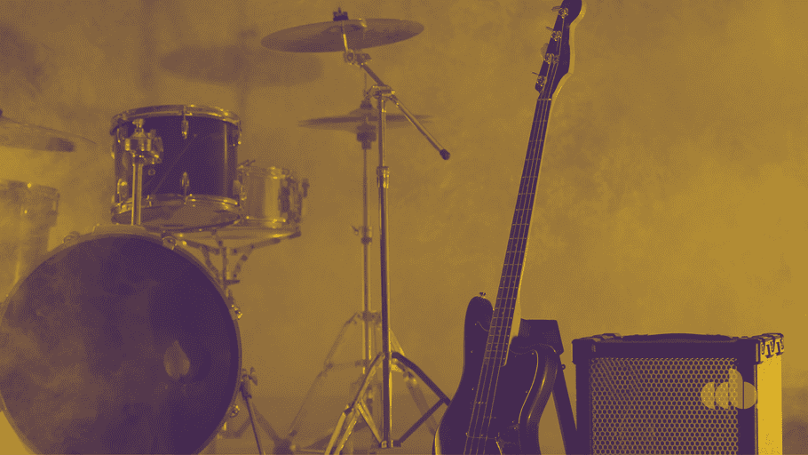 Electric guitar, drum set, and amplifier on stage with yellow lighting at a live music venue.