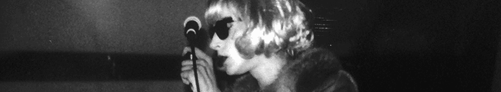 A vintage black and white photo of a woman with sunglasses singing into a microphone, capturing classic music performance moments.