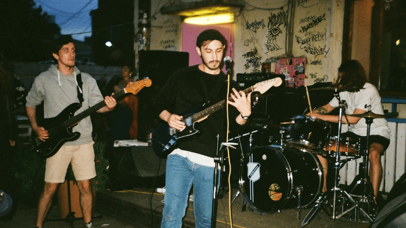 Live band performing outdoors at a music venue, young musicians playing electric guitars and drums, night setting, vibrant street graffiti background for music industry, live music, artists, performance, entertainment, Hypebot.