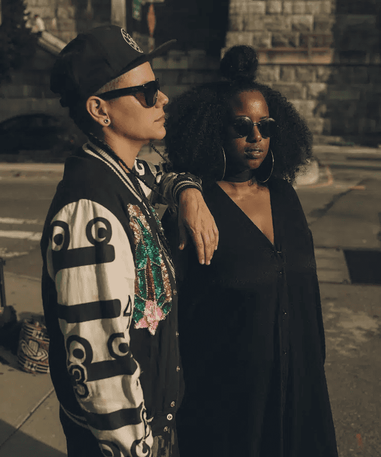 Hypebot, music lovers, urban street style, fashionable women, sunglasses, nighttime city background, diverse friends, casual attire, outdoor city scene, social gathering, street fashion, music culture, nightlife, anonymous, stylish photography.