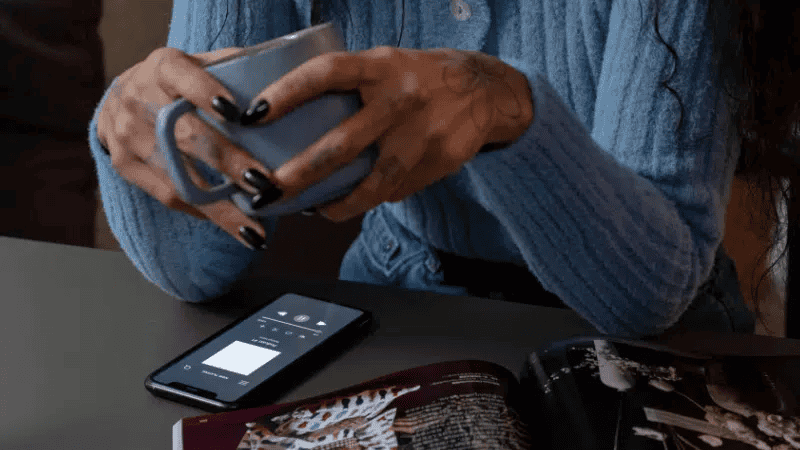 Hands holding a smartphone, browsing social media or emails, with a magazine and tablet nearby, capturing a modern digital lifestyle.