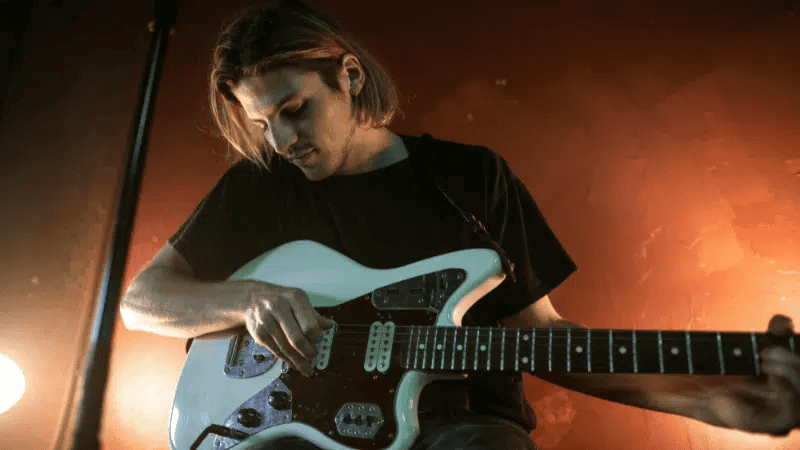 Guitarist playing electric guitar on stage at music concert, live performance, musician with intense focus, stage lighting, rock music, Hypebot music industry news, artist branding, music marketing.