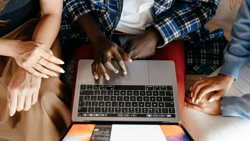 Hands of diverse people working together on a laptop at a collaborative meeting or discussion.