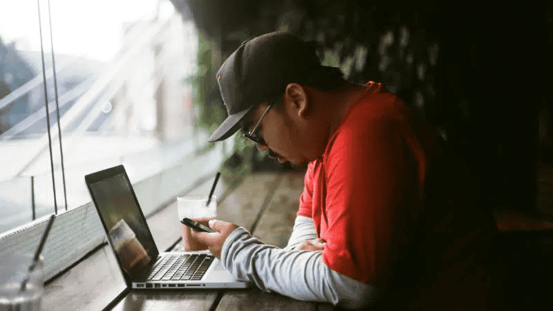 Laptop and smartphone user working in a cafe, focused on digital content creation and music industry insights.