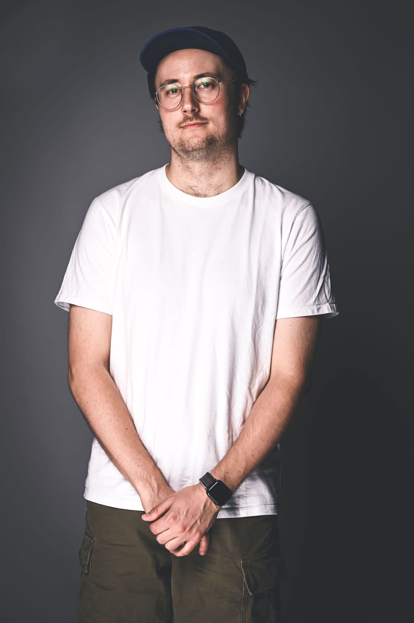 Professional music industry analyst wearing casual white t-shirt, dark-rimmed glasses, and a cap, standing against a neutral gray background for Hypebot imagery.
