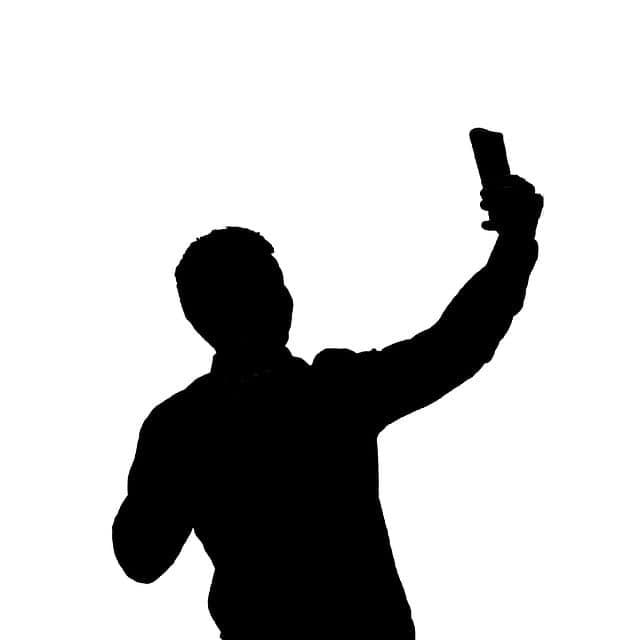 Silhouette of a person taking a selfie with a smartphone, highlighting social media engagement and digital content creation.